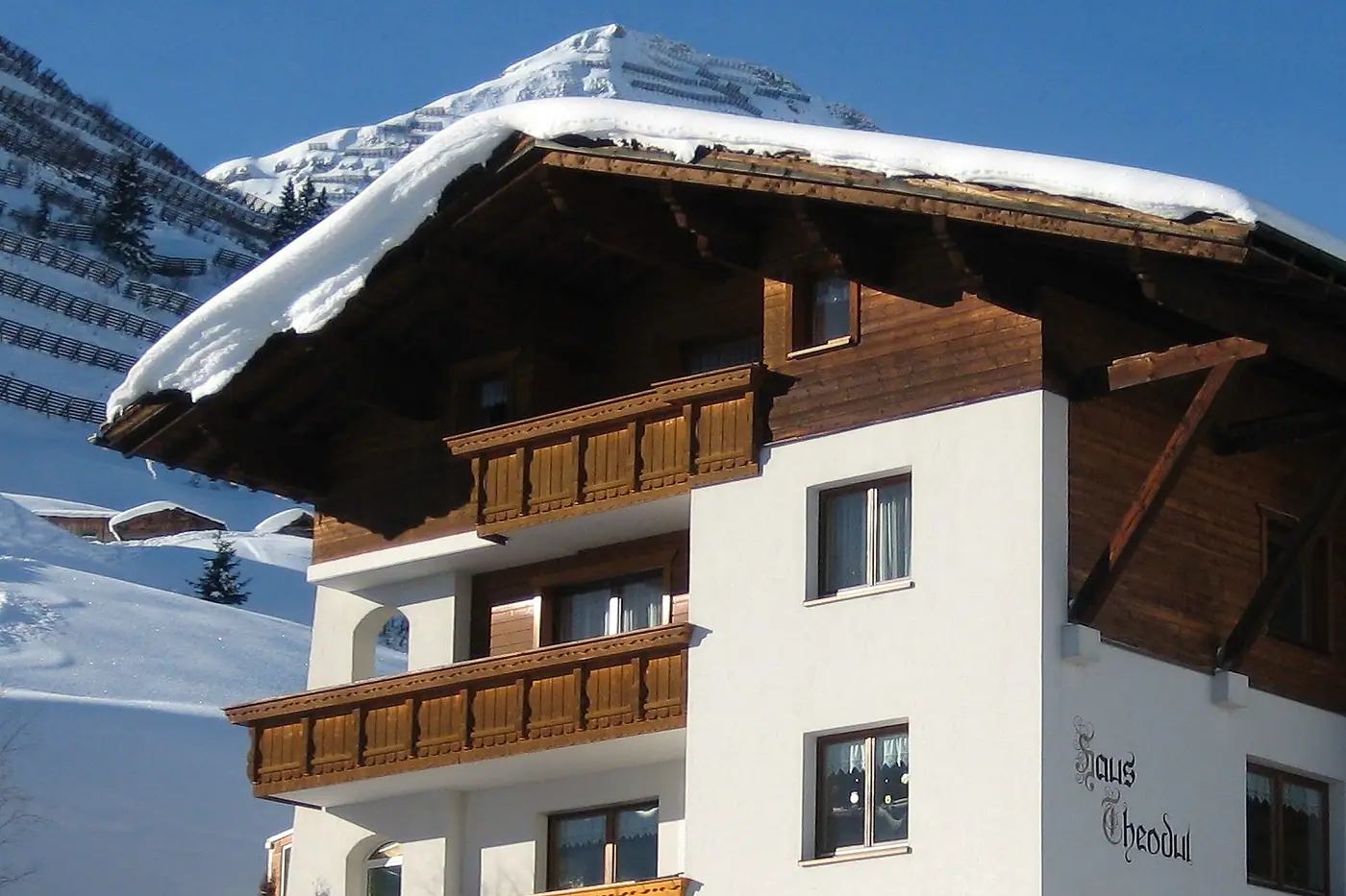 Holzbalkone und tief verschneites Dach von Haus Theodul, dahinter ein Gipfel im Schnee